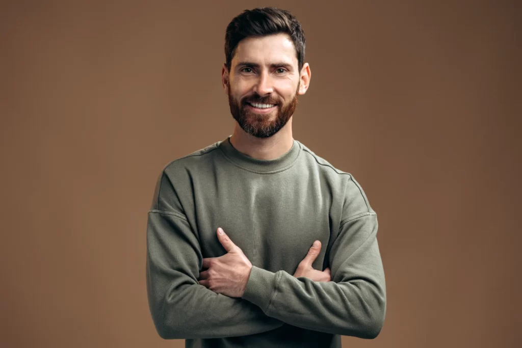 man smiling with arms crossed against brown backgr utc