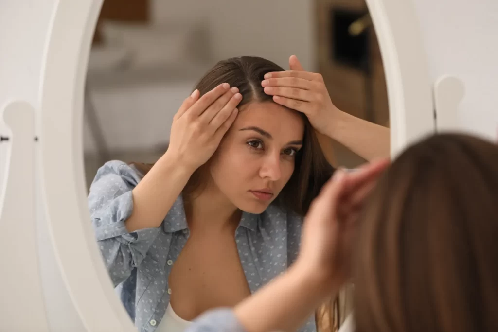 young woman examines hair in mirror indoors utc
